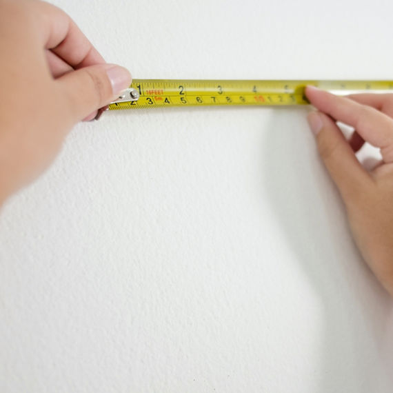 Hands of woman using measuring tape on white wall.