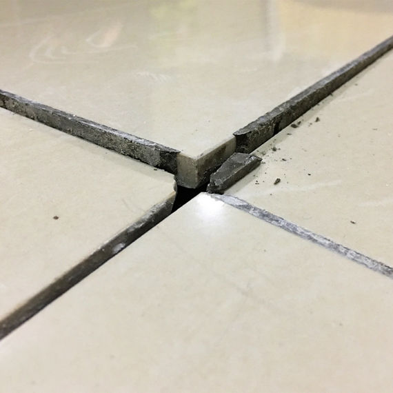 Close up of a cracked ceramic tiles on a residential house floor surface due to improper construction material.