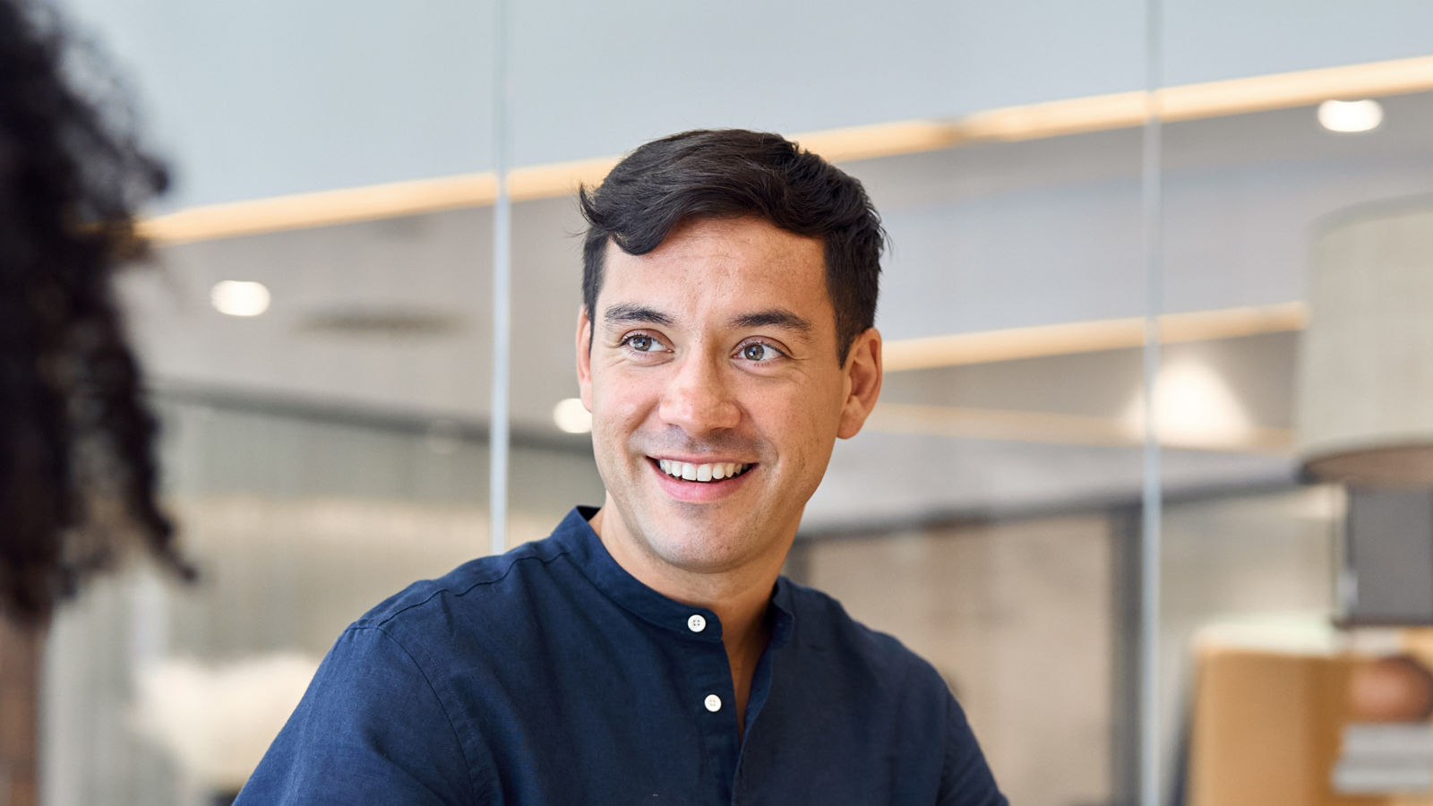 Young professional Hispanic business man manager talking to female colleague or consulting client at corporate meeting. Busy business team people working together using laptop in office. Vertical