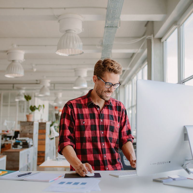 Shot of happy young man working on desktop computer in modern workplace. Young entrepreneur working at start up.