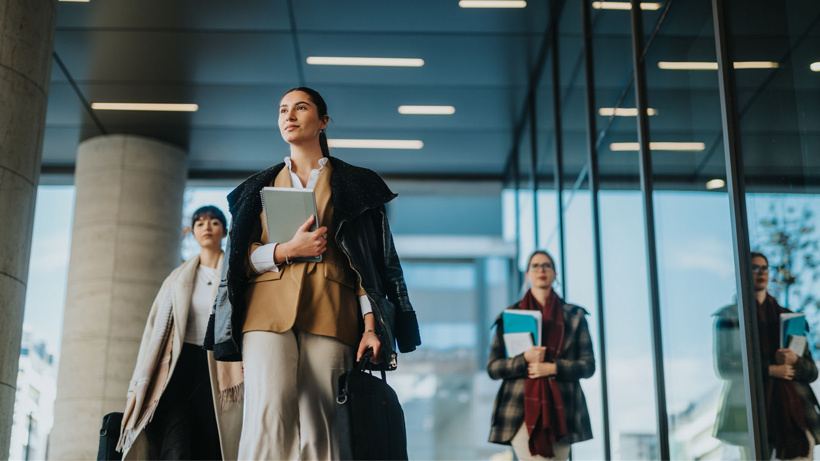 A group of professional women walking confidently through a modern urban area, holding documents and symbolizing collaboration, success, and professionalism in a business-oriented outdoor setting.