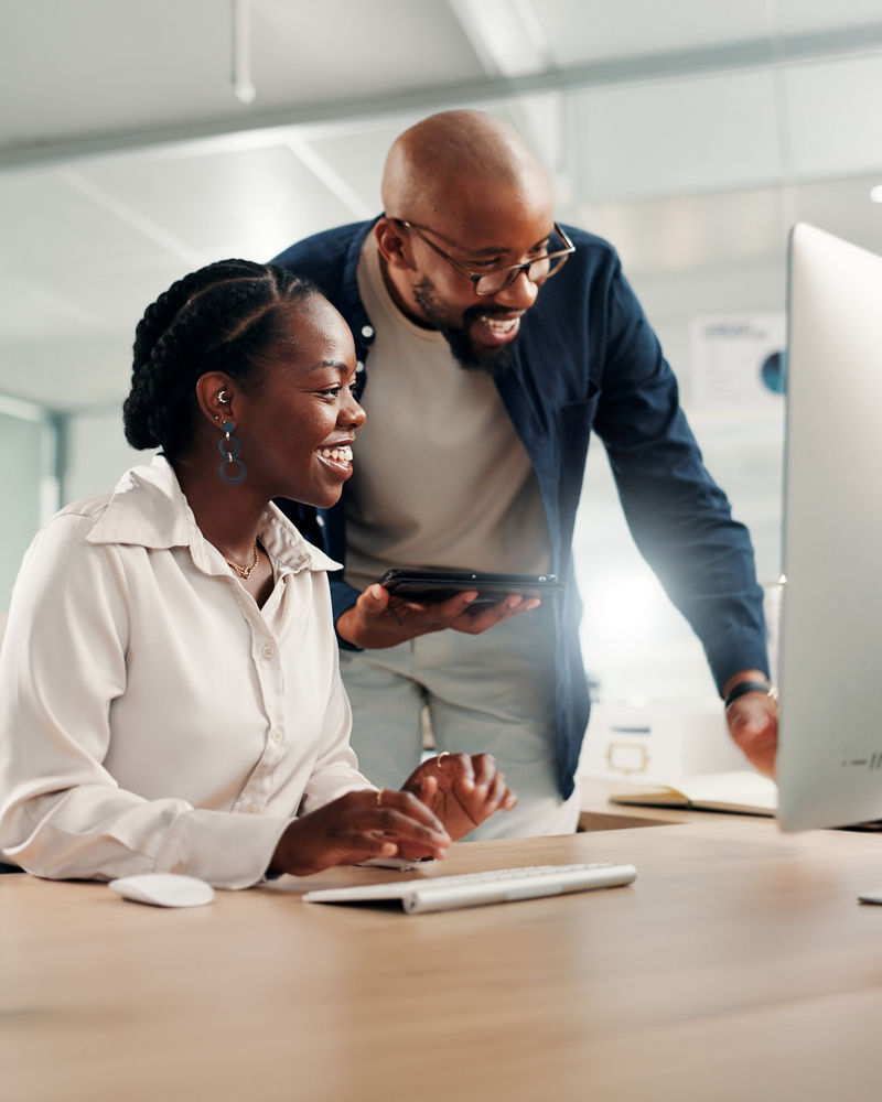 2 sales people looking at computer smiling in office