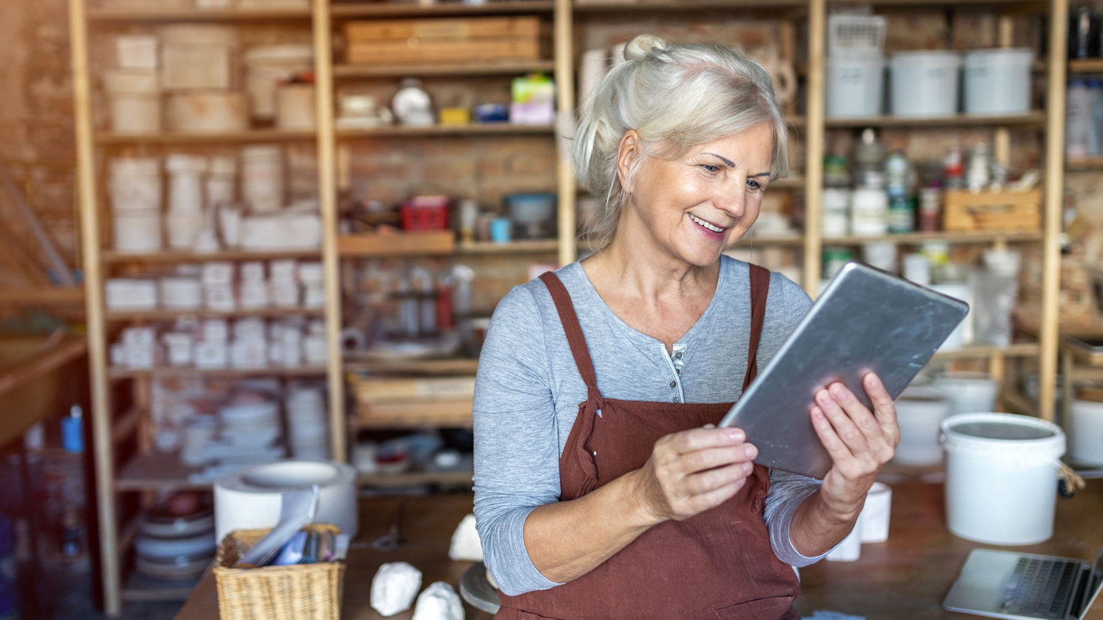 Caucasian businessman is sitting in an office and having a meeting with a female colleague. He might be working from home. It's morning or later in the day. He is smiling. A laptop is in front of him and the woman is holding a digital tablet.