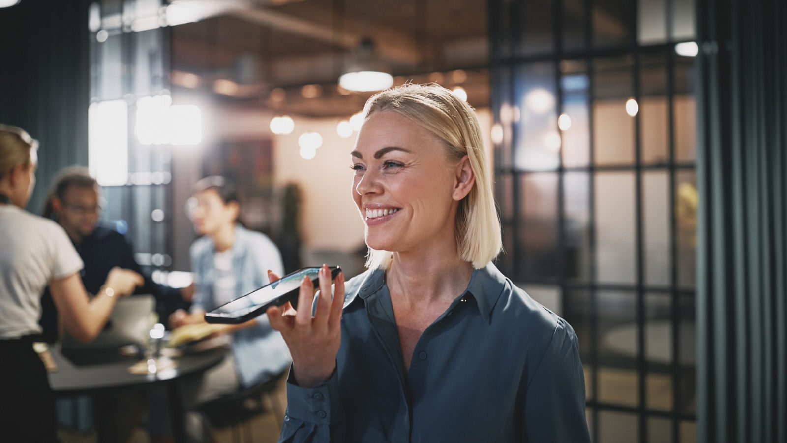 Laughing young businesswoman talking with a client on speakerphone while working late in an modern office