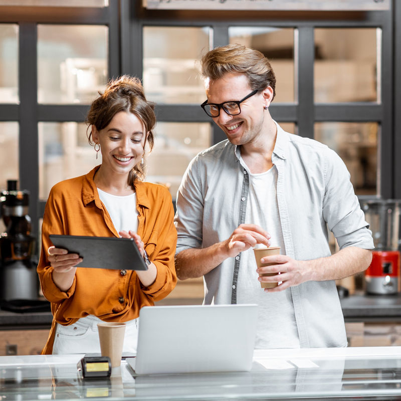Two young managers or shop owners having some discussion while standing with a digital tablet at the counter of the shop or cafe. Small business management concept