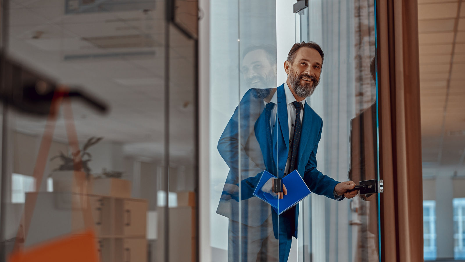 Smiling Caucasian man entering office space and holding notepad, copy space