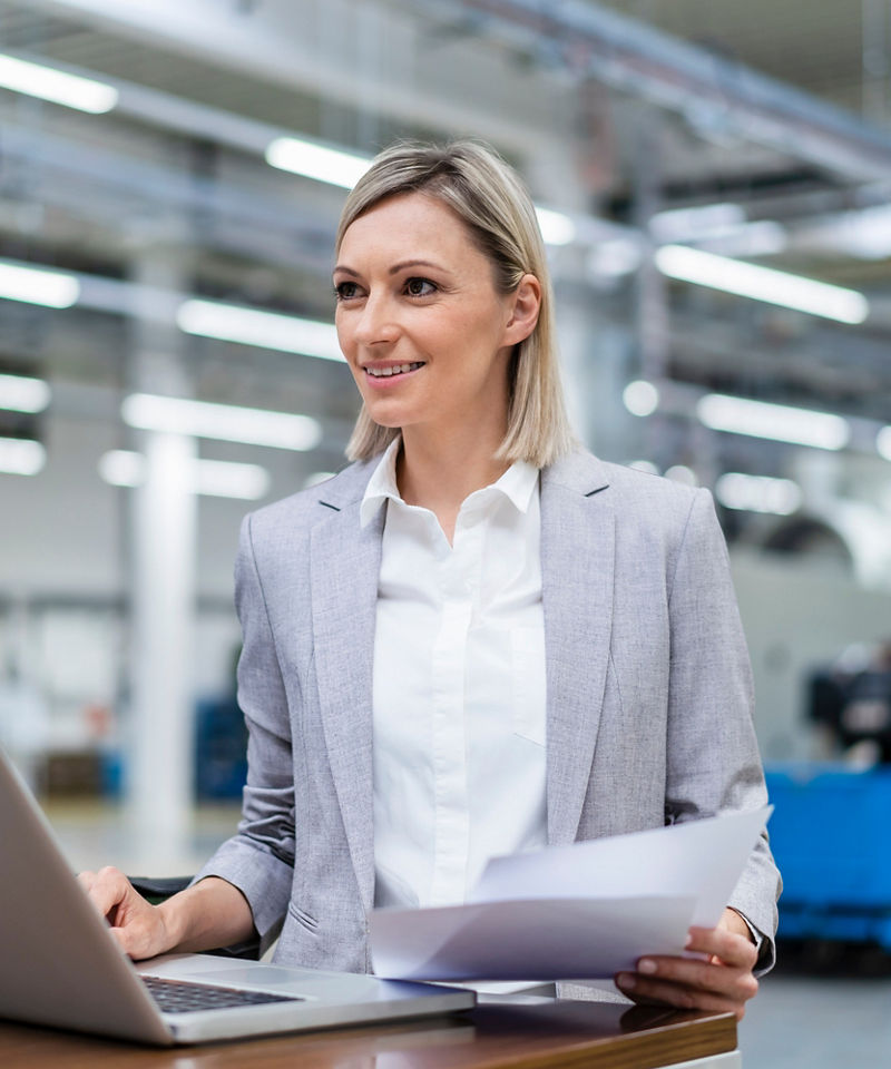 Smiling businesswoman with laptop and documents in factory