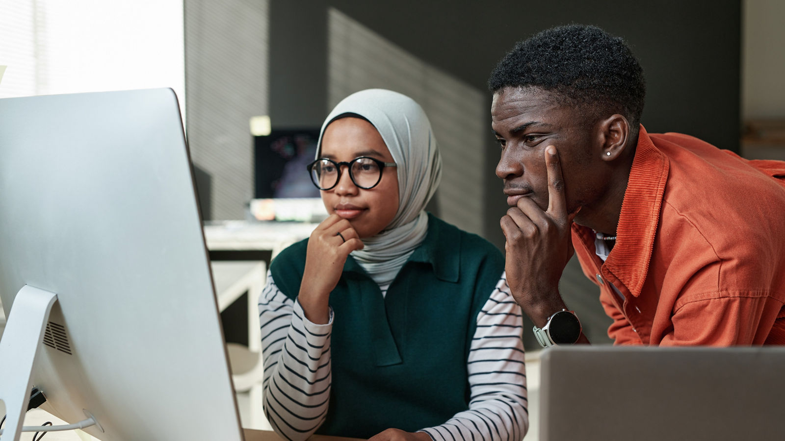 Two young professionals contemplating information shown on a computer screen in an office.