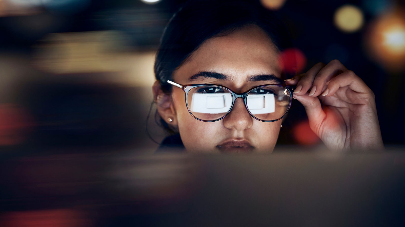 Woman, glasses reflection and computer at night for planning, website search and technology. Face of female working late on desktop, dark office and reading online network, focus vision and internet.