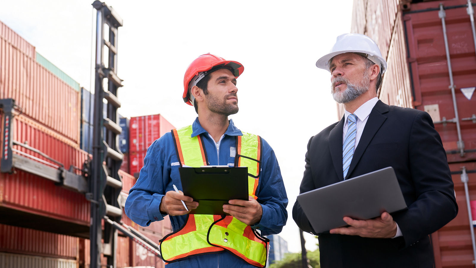 Foreman discussing with inspector manager for checking plan to shipping container box  to customer in logistic service by laptop.