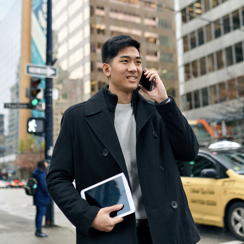 A business man office professional holding cellphone in hands walking on big city urban street making corporate business call, talking on cellular phone standing in downtown.