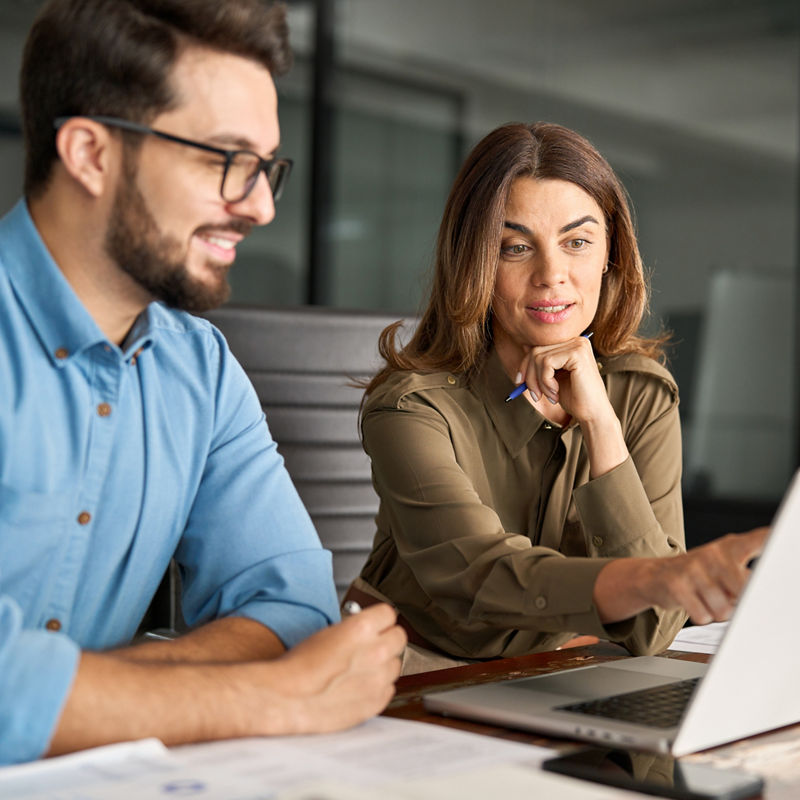 Busy female manager explaining corporate work talking to young male employee consulting client working on computer at office meeting.
