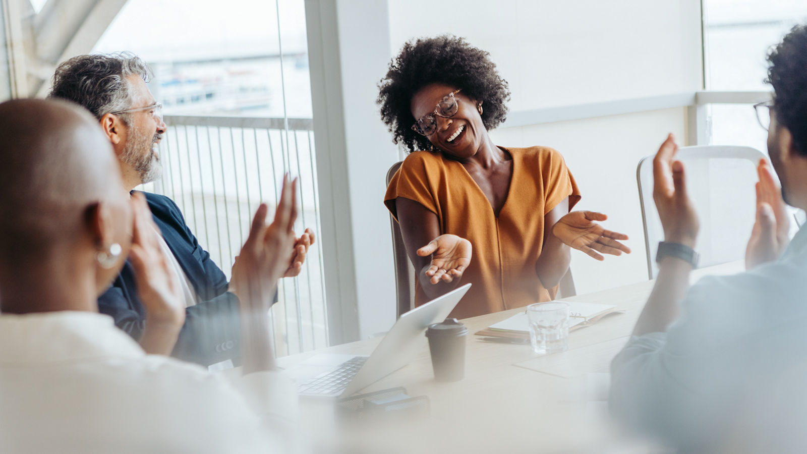 Group of business people in a bright boardroom clapping and celebrating their successful project. This collaborative team of men and women showcases teamwork and professionalism in their workplace.