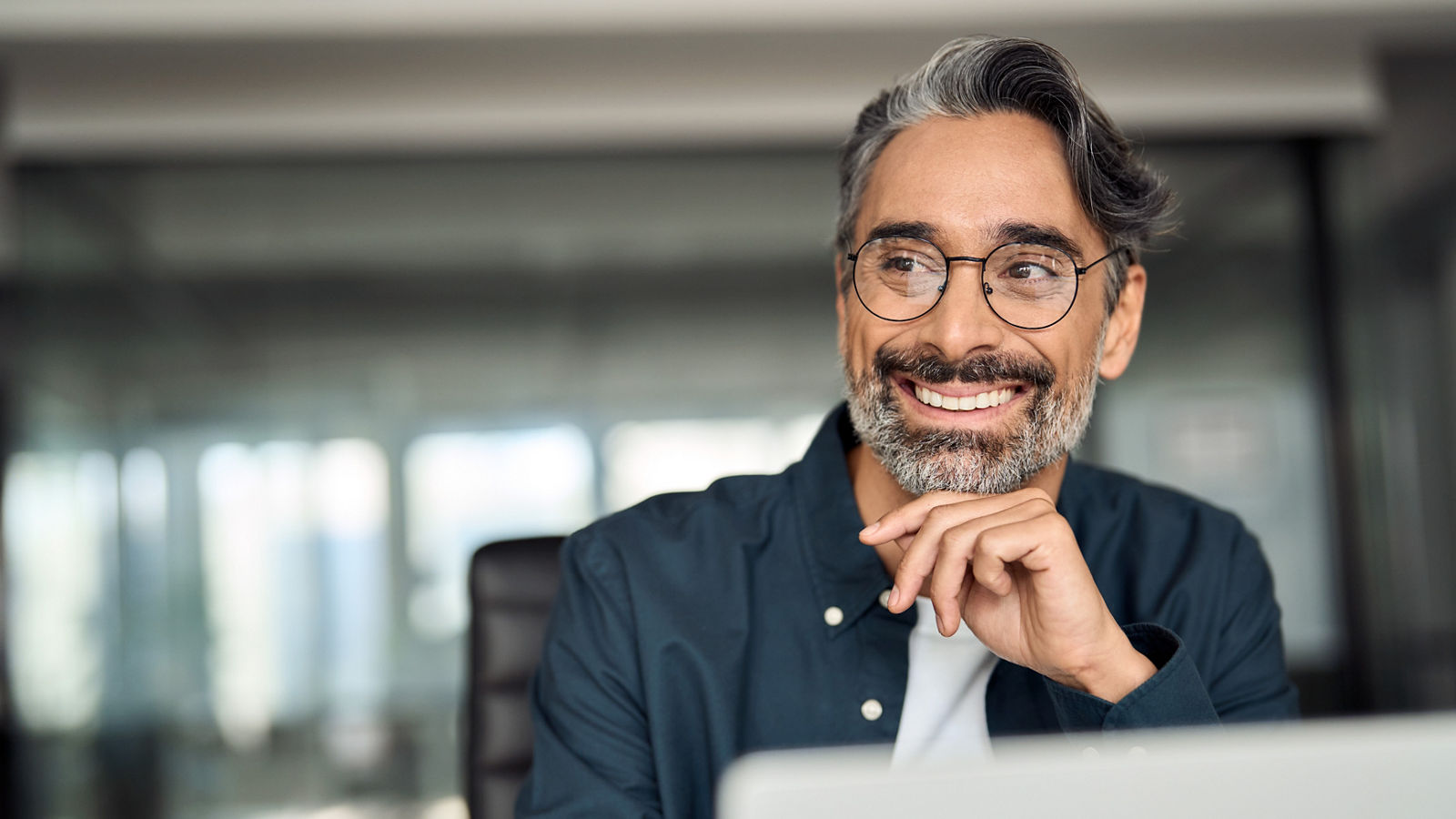 Smiling confident business man sitting at desk using laptop.