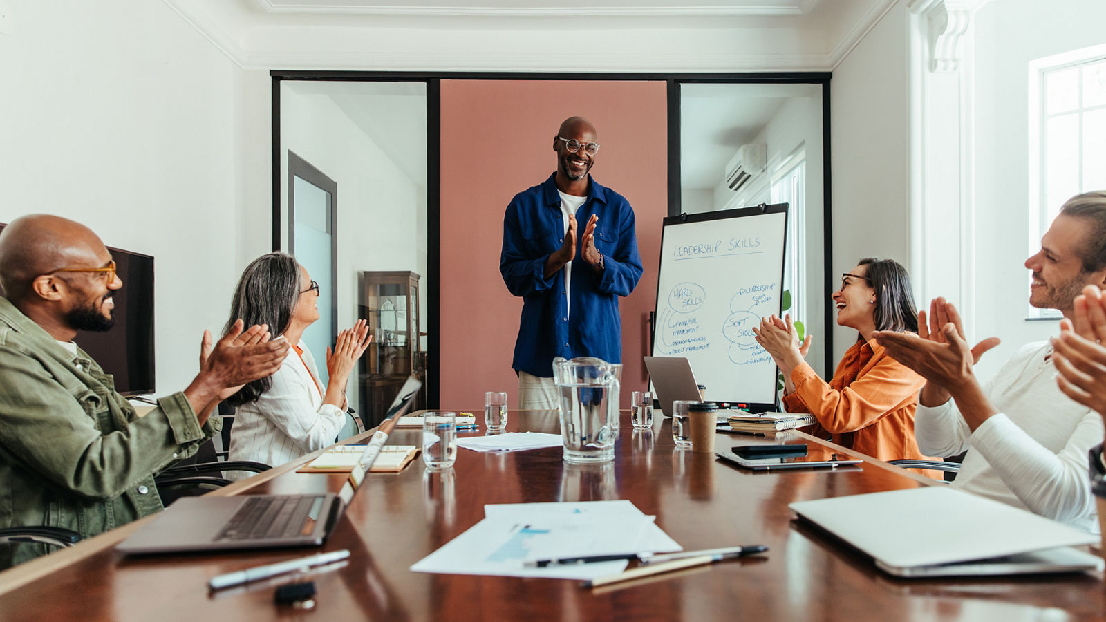 Diverse business team applauding a successful presentation led by a confident leader in a modern office meeting room.