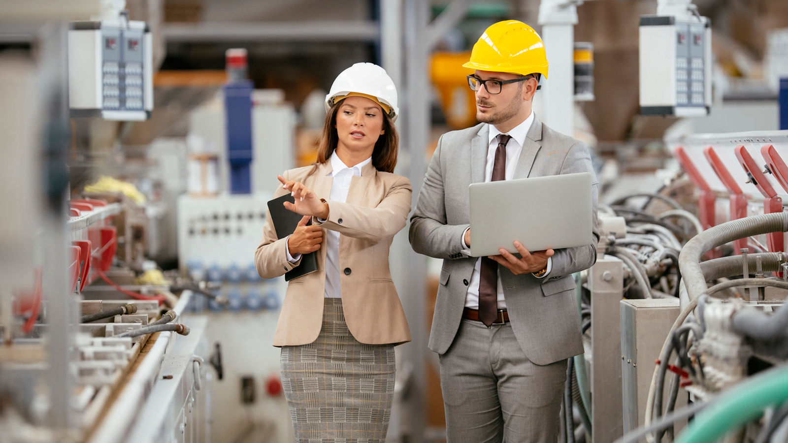 Businessman and businesswoman in factory. Two professional people with helmets working in quality control in factory production line.