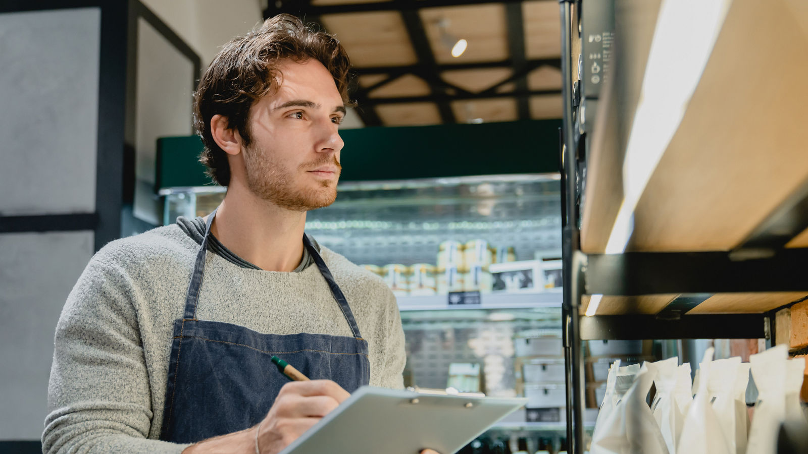 Young handsome caucasian waiter checking the quality of goods holding a folder in cafeteria