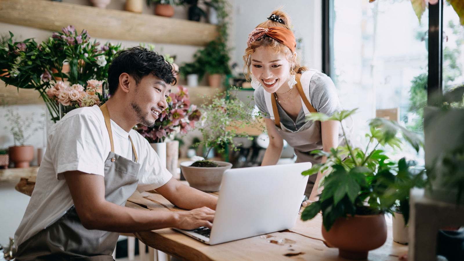 Small business owners in florist shop looking at laptop smiling