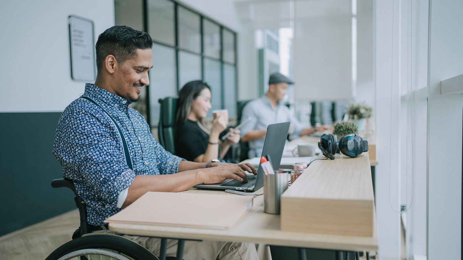 Man in wheelchair working on laptop in office smiling