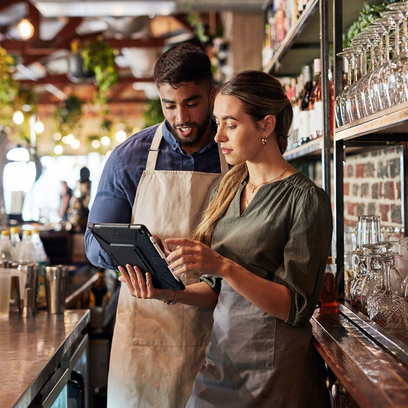 Small business owners looking at tablet inside of restaurant bar