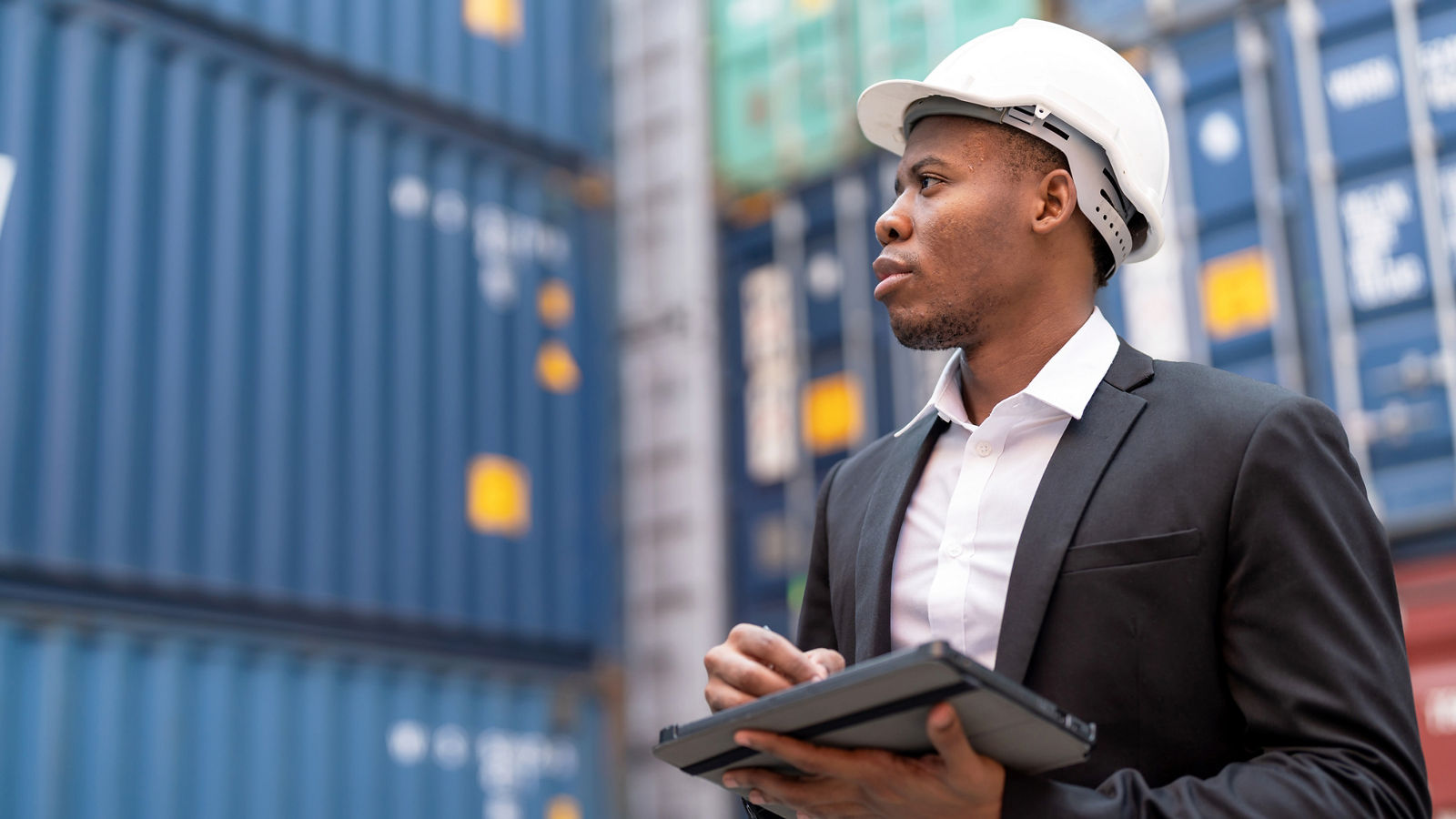 Business man in front of shipping containers with tablet