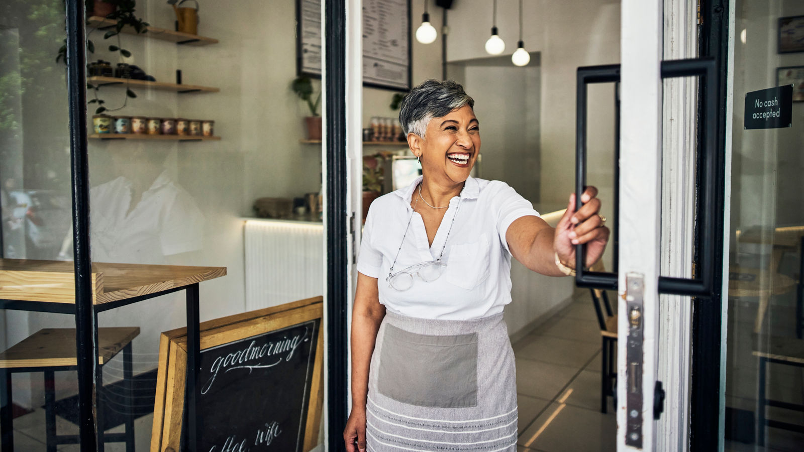 Small business owner opening door of coffee shop smiling