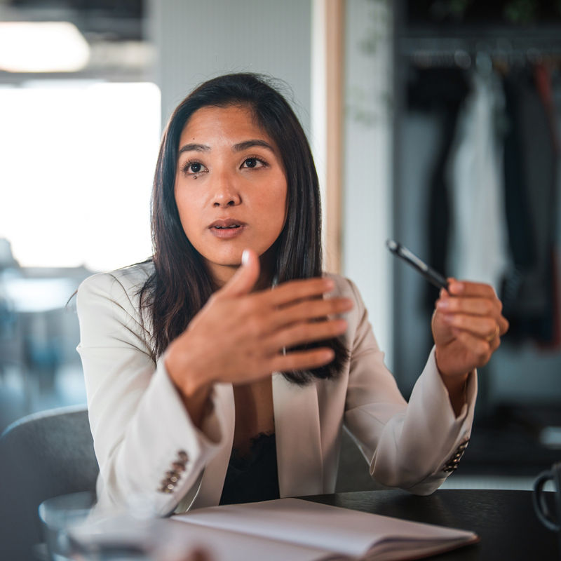 Waist up shot of japanese businesswoman talking using her hands. She has dark short hair and looks at male coworker.