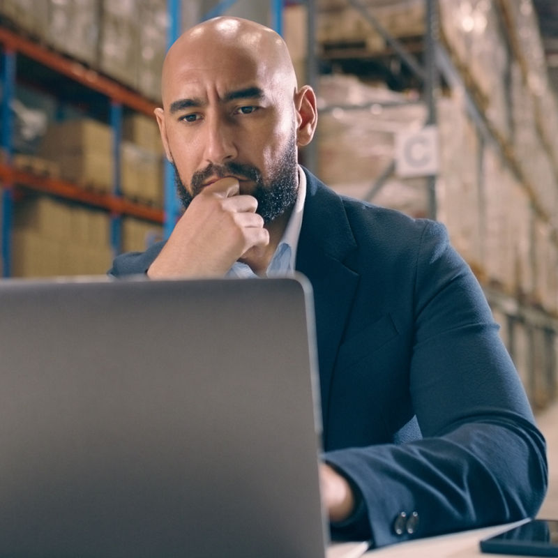 Thinking, logistics and man on laptop in warehouse for ecommerce delivery stock inventory. Networking, communication and male industry worker typing to respond to email on computer in cargo factory.