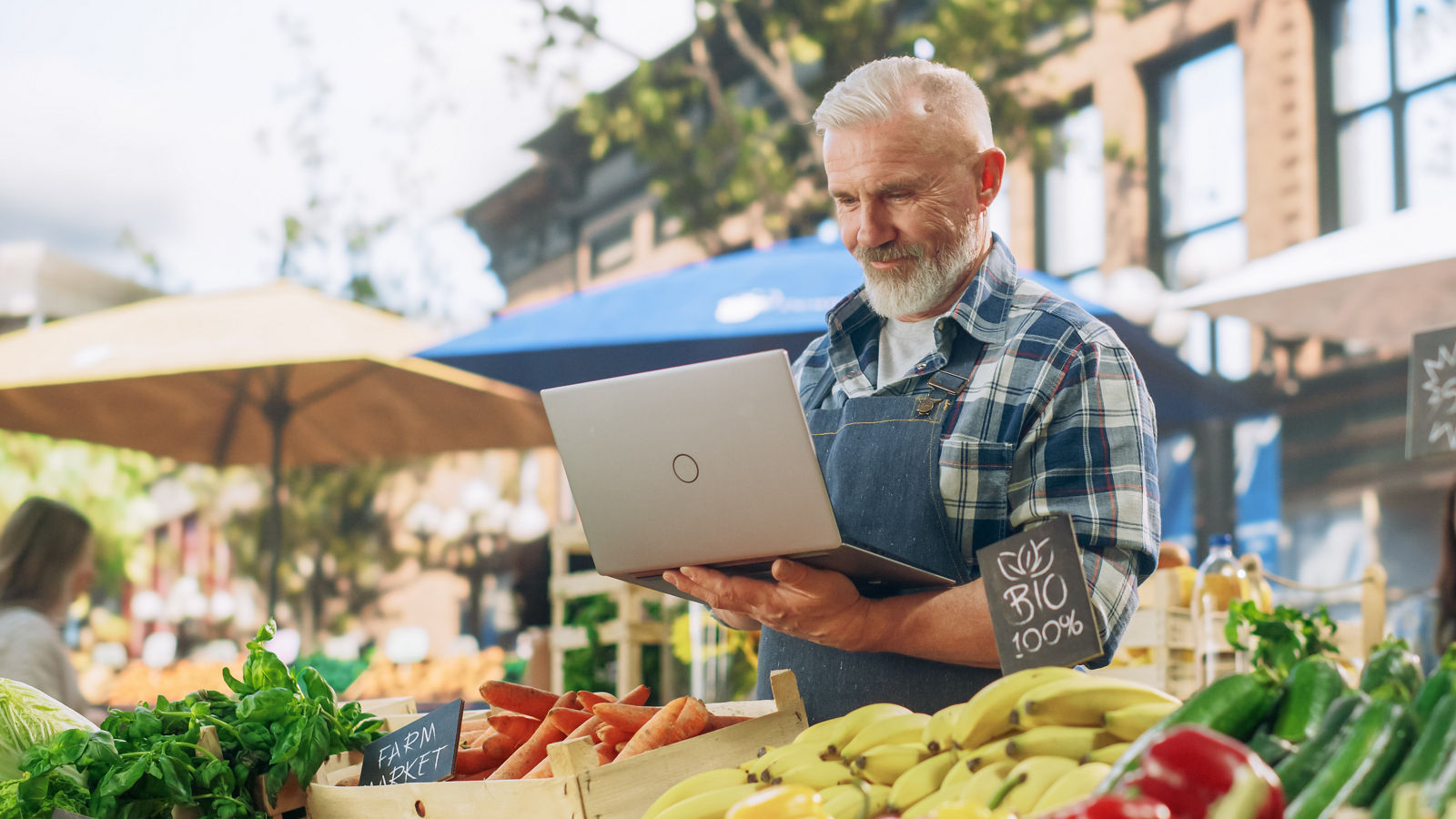 Caucasian businessman is sitting in an office and having a meeting with a female colleague. He might be working from home. It's morning or later in the day. He is smiling. A laptop is in front of him and the woman is holding a digital tablet.