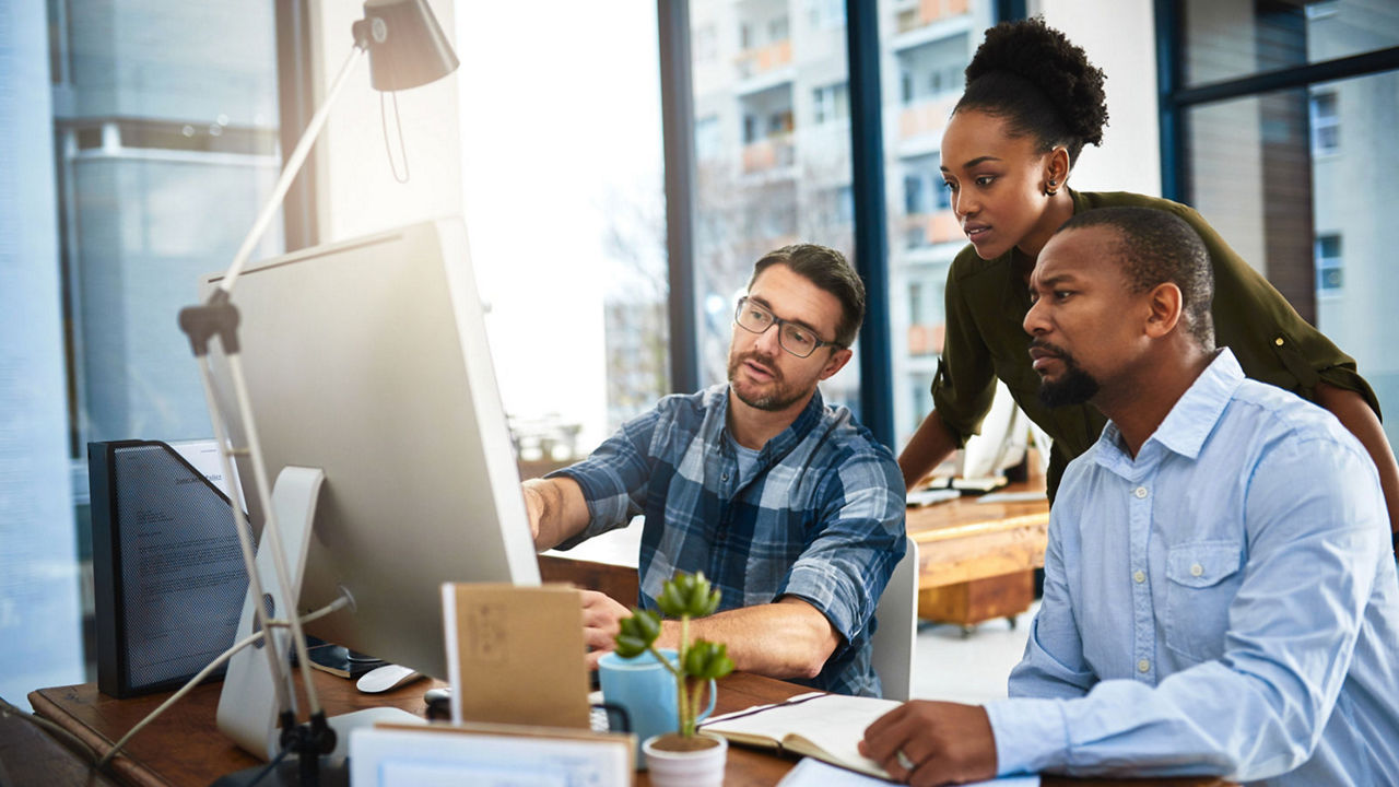 Three business people working around a computer in the office
