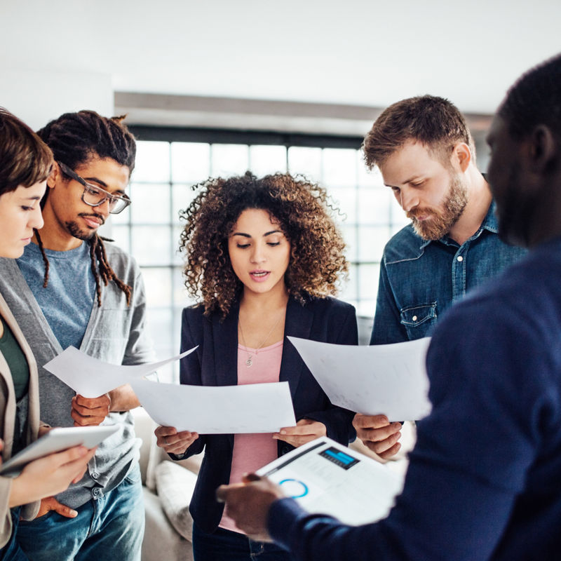 Young woman with colleagues reading a contract. Young people going through contract papers at startup.