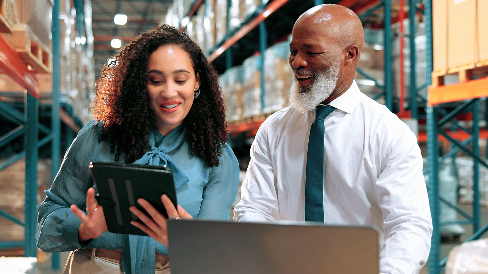 A picture of two procurement managers looking at a tablet and laptop in a warehouse