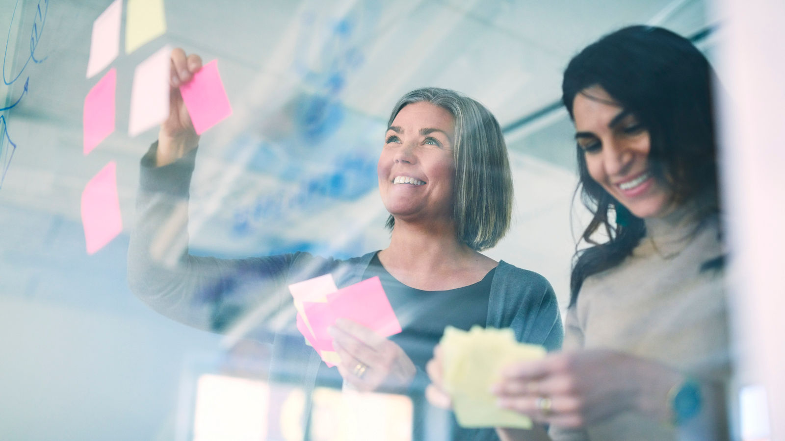 Low angle view of business professionals smiling while sticking adhesive notes on glass in office