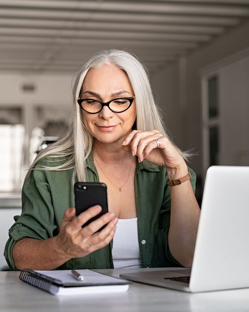 Business woman using mobile phone while working with laptop.