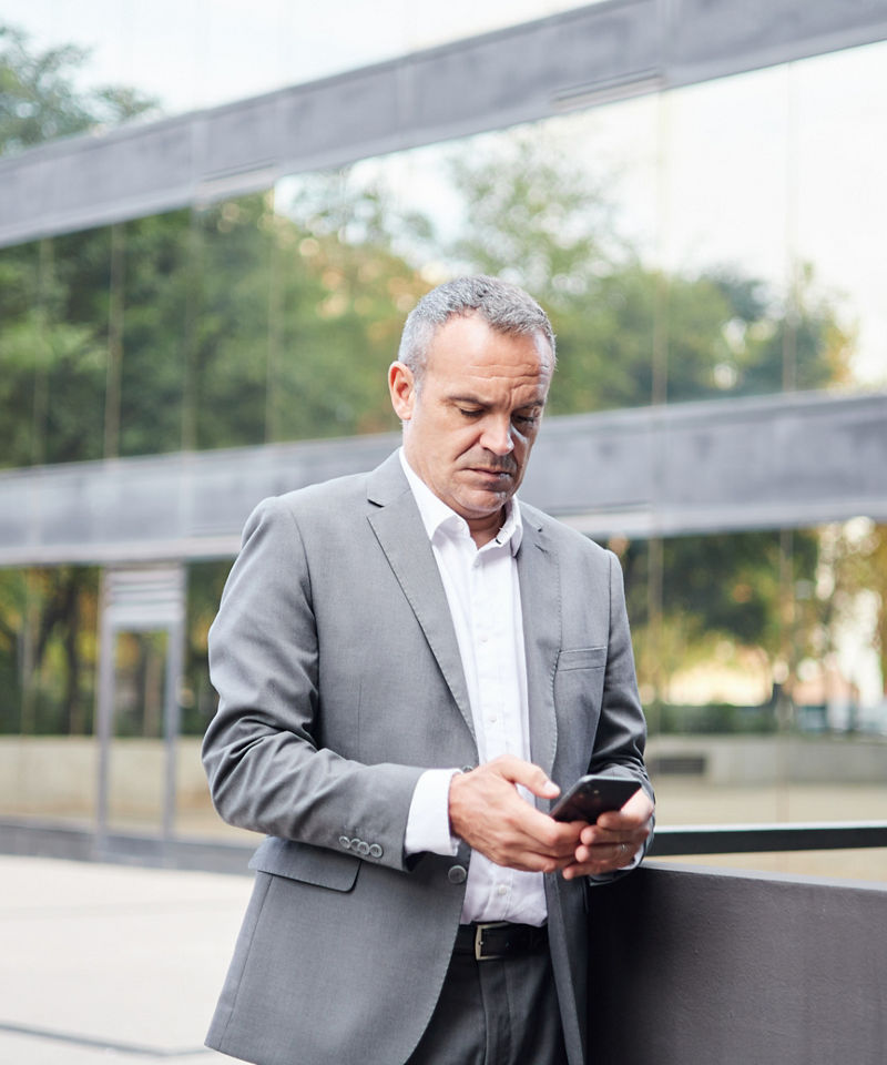 Przedsiębiorca korzystający z telefonu komórkowego przed nowoczesnym budynkiem przy ulicy w mieście 