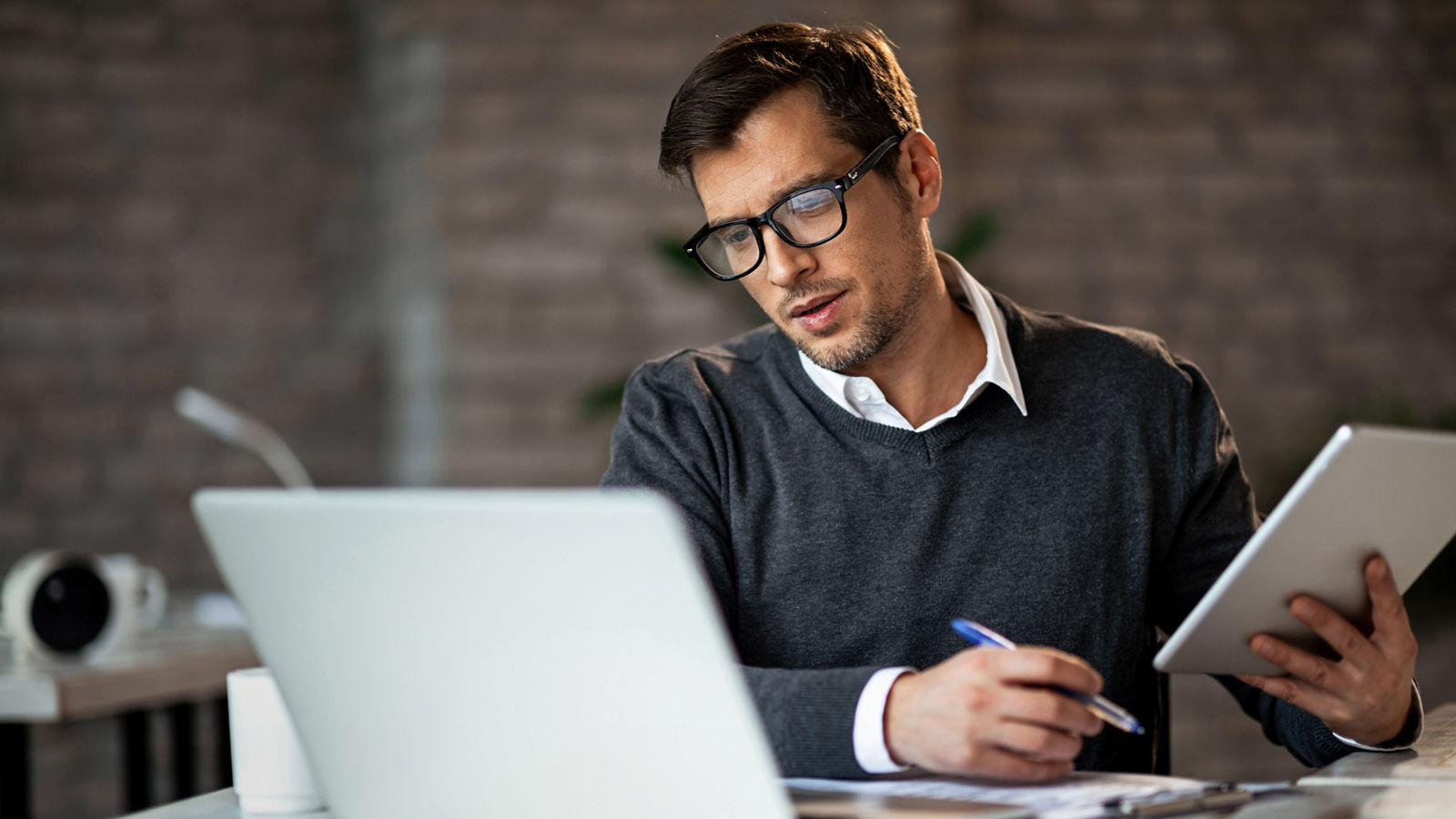 Multi-tasking businessman working in the office. He is using touchpad while reading an e-mail on laptop and taking notes on the paper.; Shutterstock ID 1350370946; purchase_order: 2024-10; job: Guide; client: ; other: 