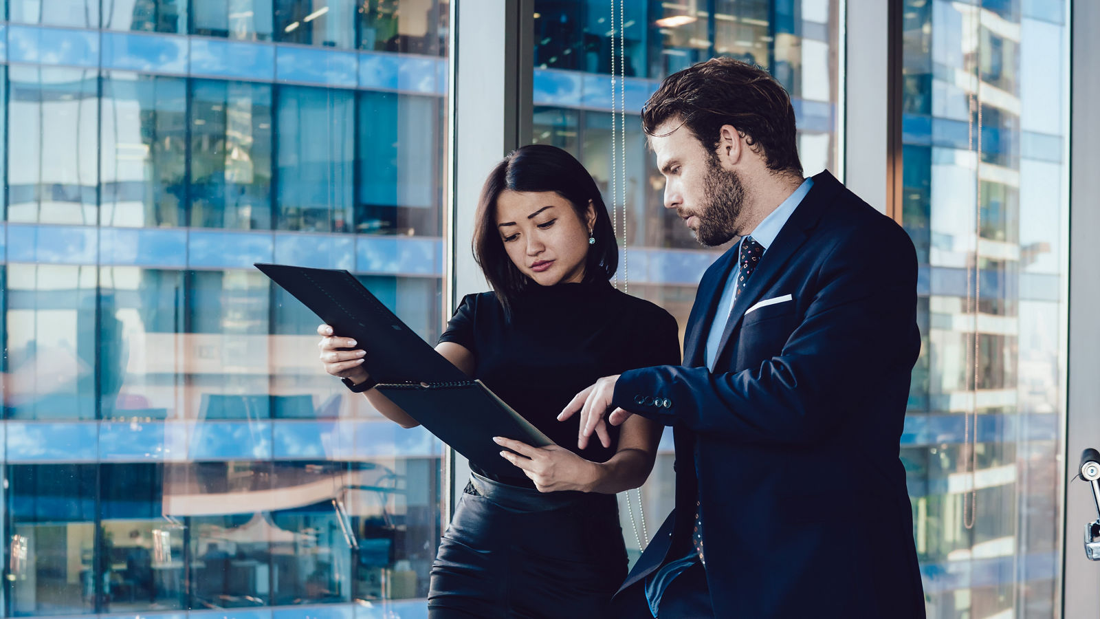 Young professional caucasian male and and female colleagues discussing working planning together walking in office, skilled woman assistant showing documents to man ceo of company discussing financial strategy