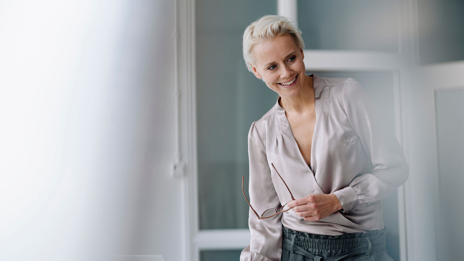 Smiling businesswoman looking away while using laptop against wall in office