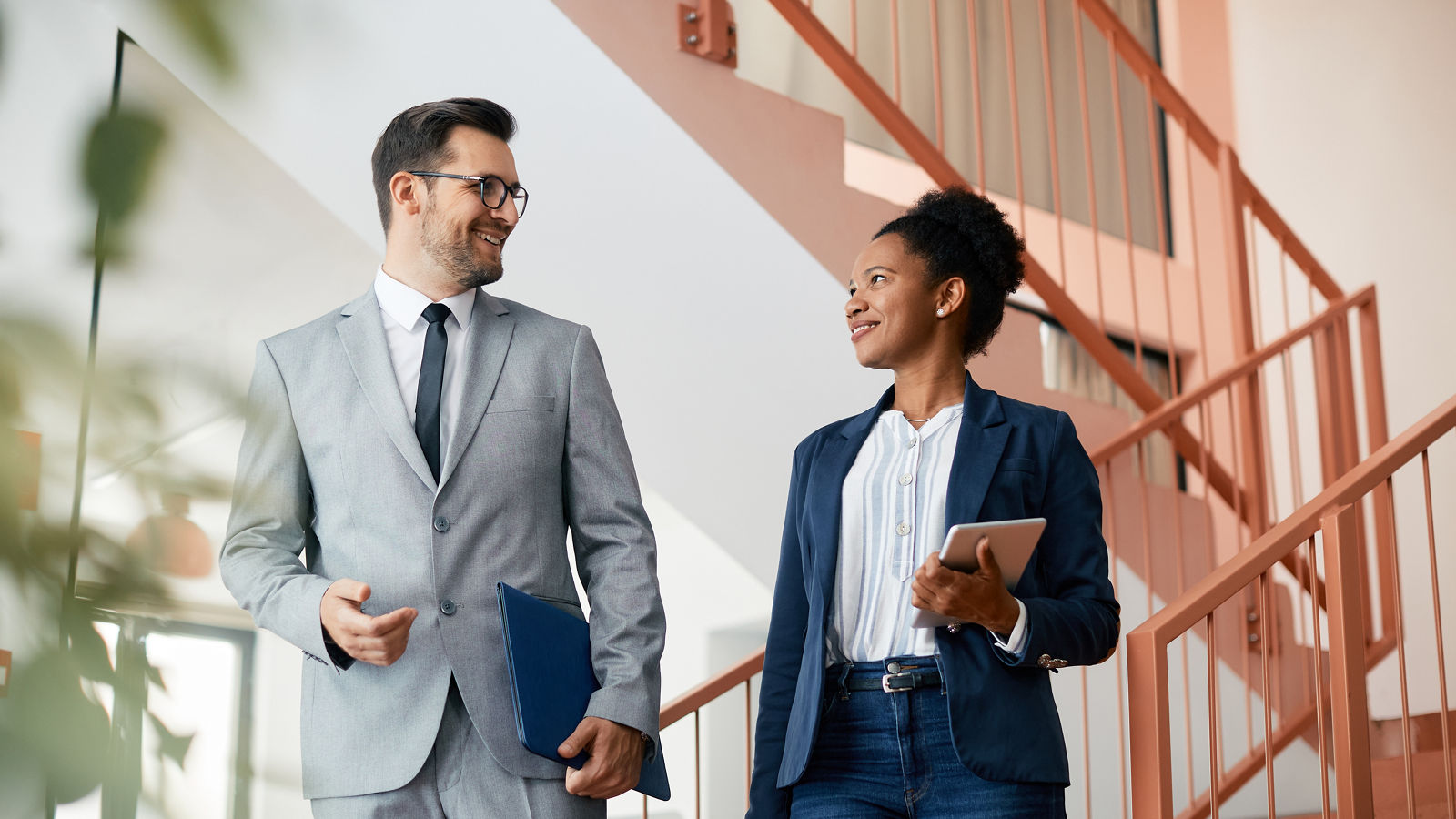 Happy business colleagues talk while walking through corridor of an office building.