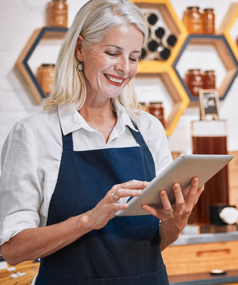 Happy woman small business owner using tablet in honey store