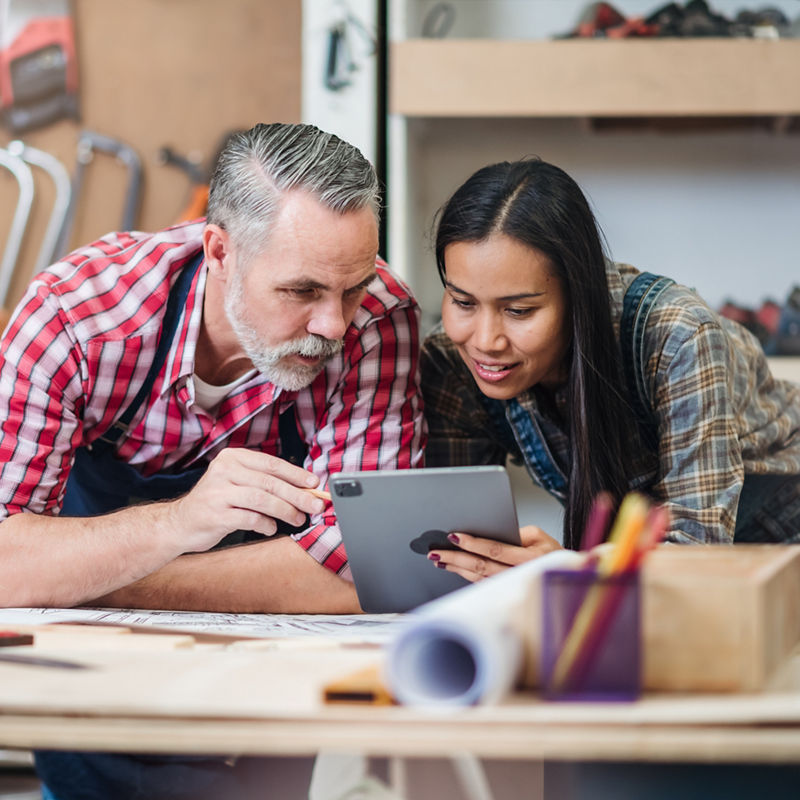 Small business furniture owner and professional architect interior designer working in carpenter workshop with blueprint and tablet discussing about home furnishing design project.