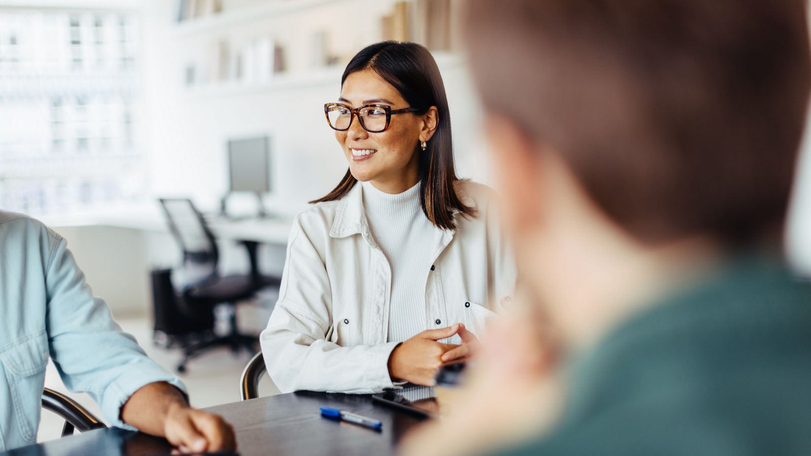 Business woman sitting around a table and listening to a discussion in an office. Female professional having a meeting with her team.