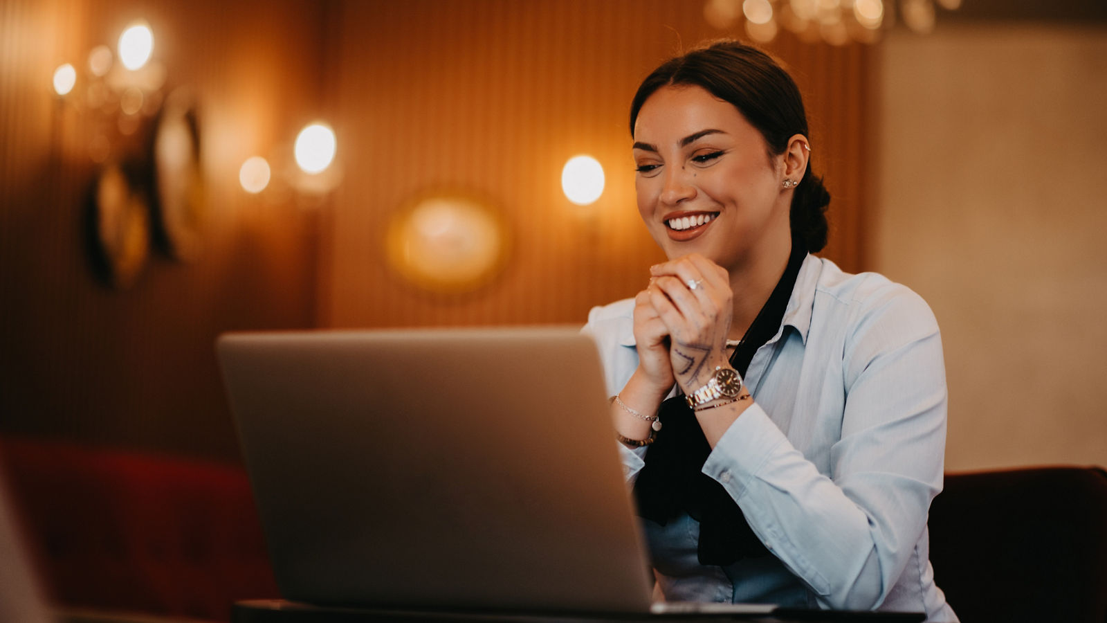 A charismatic Latina businesswoman confidently engages in a business meeting at a cafe, her laptop screen reflecting her presentation. 