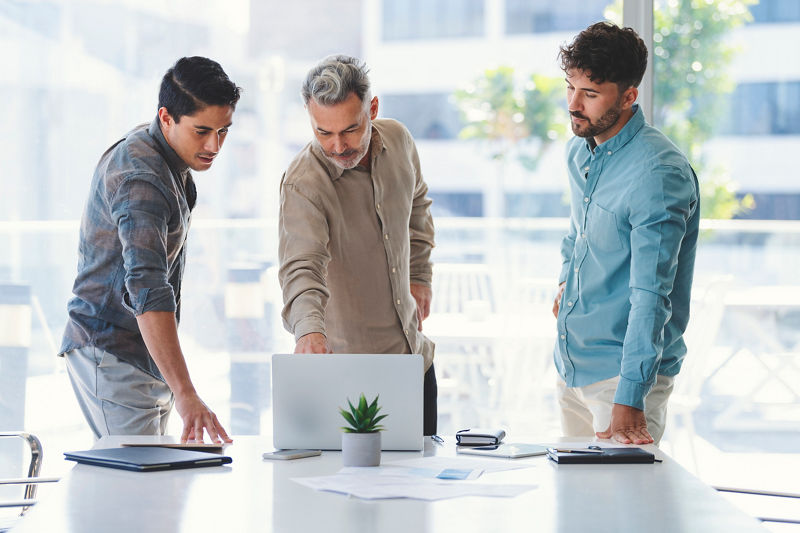 Three businessmen standing looking at a laptop computer. 