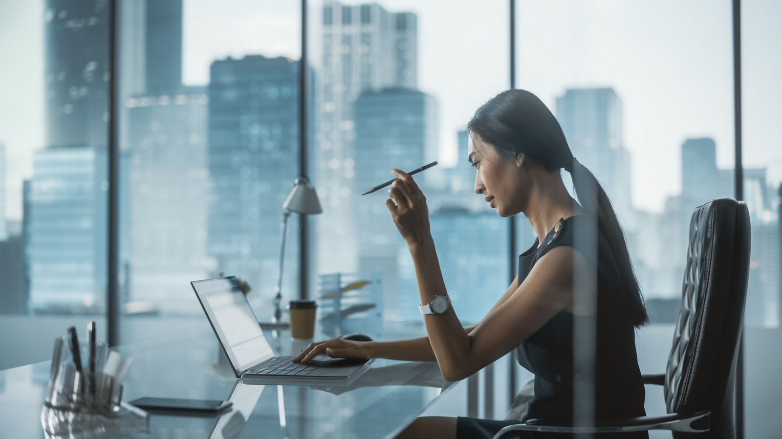 Businesswoman Sitting at a Desk in Modern Office, Using Laptop Computer