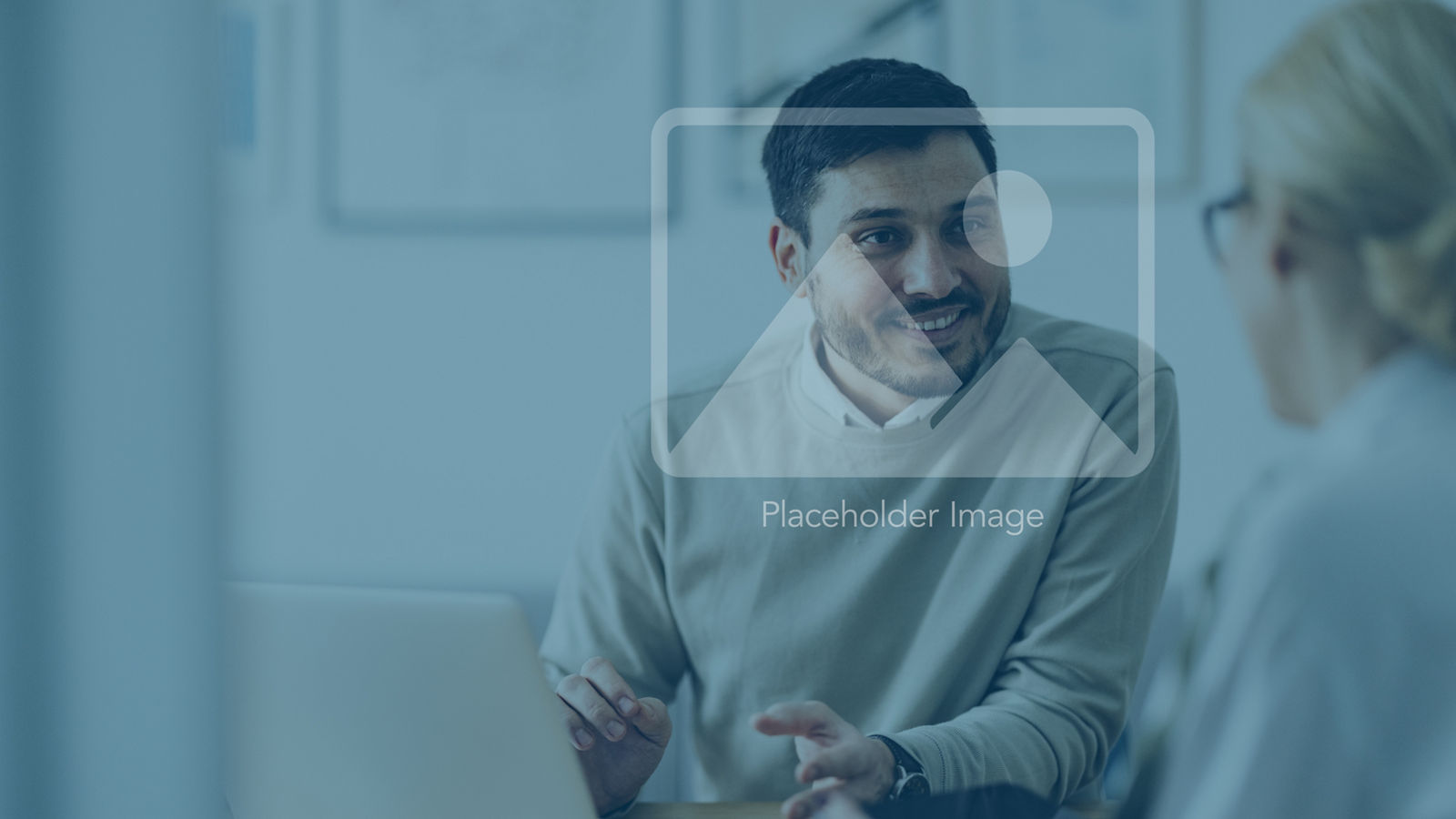 Caucasian businessman is sitting in an office and having a meeting with a female colleague. He might be working from home. It's morning or later in the day. He is smiling. A laptop is in front of him and the woman is holding a digital tablet.