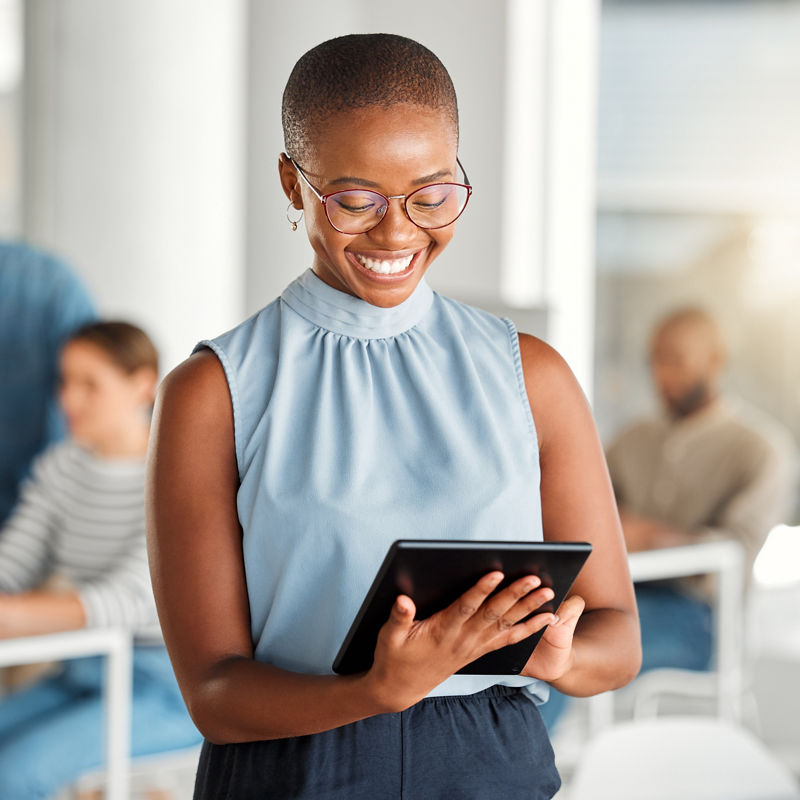 Cheerful african american businesswoman working on a digital tablet at work. Joyful black female businessperson using social media on a digital tablet. Businessperson checking an email on a digital tablet