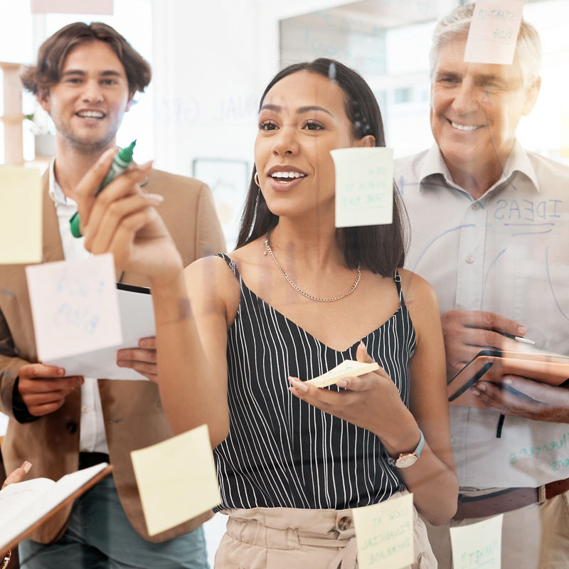 Team of workers in office, brainstorming together and writing ideas on sticky notes at glass board