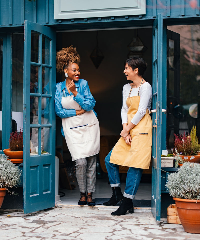Happy woman and her employee talking and laughing while standing at door of the store.
