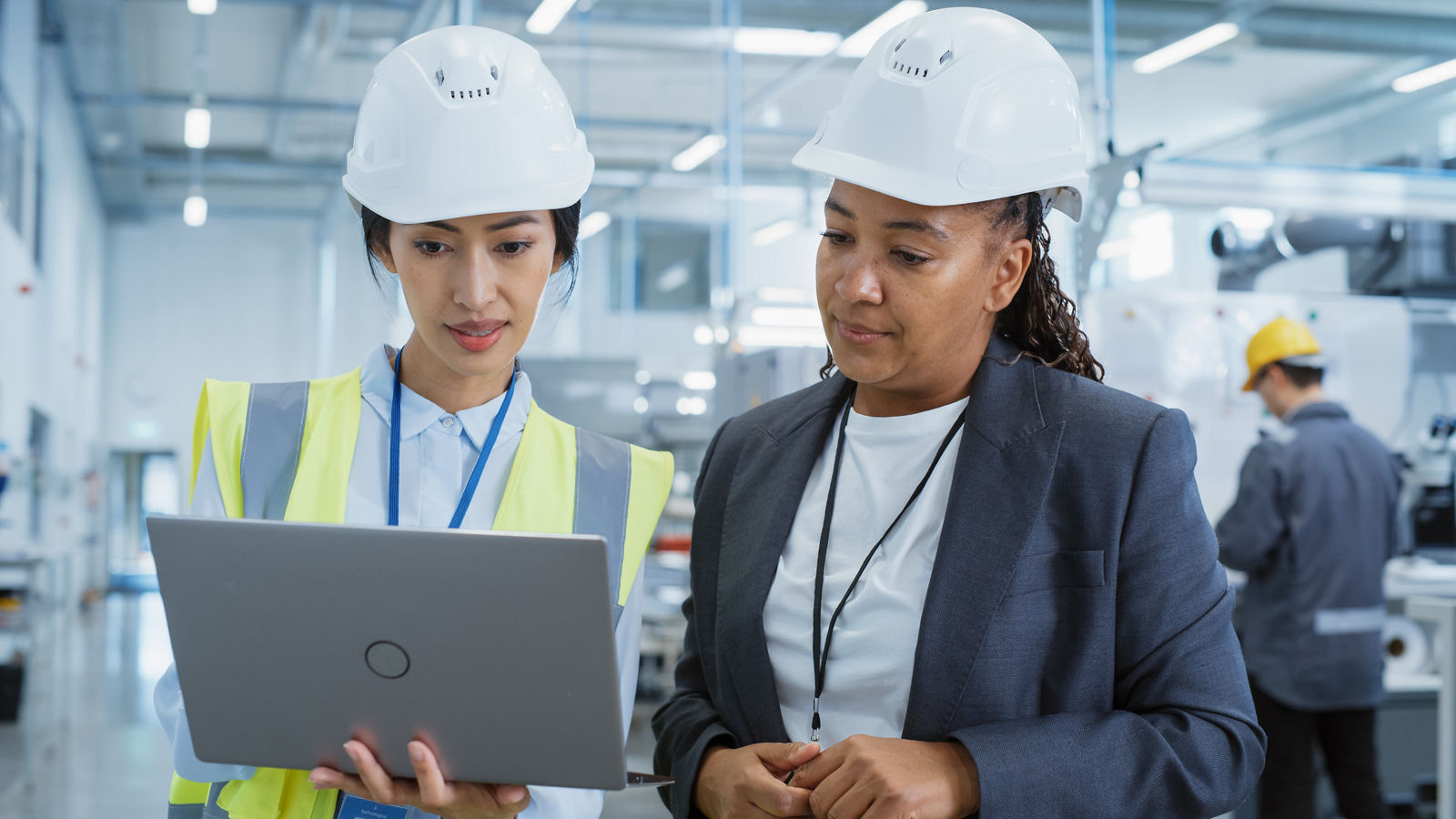 Portrait of two female employees in hard hats, discussing operational risks at a factory